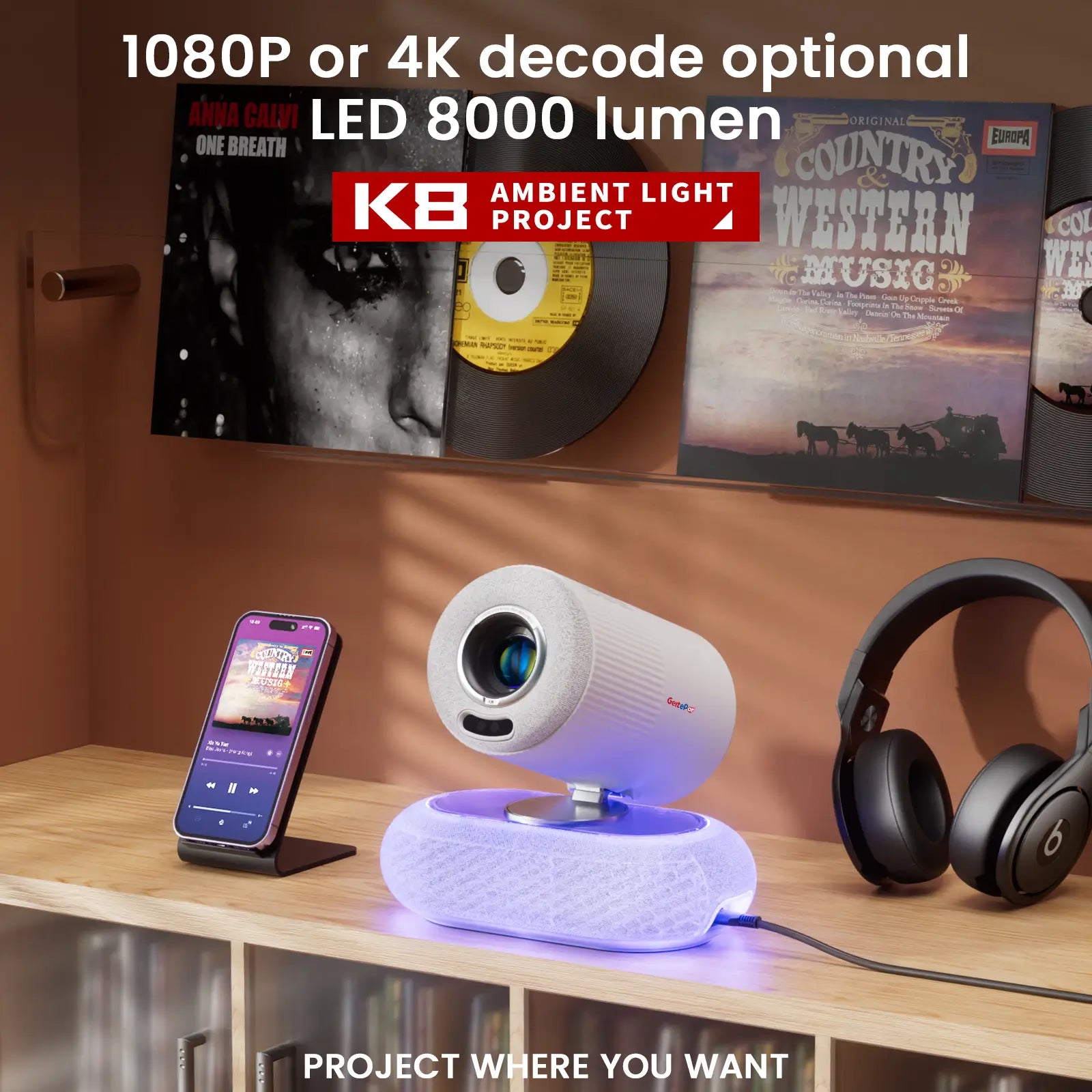 The Geitepor K8 projector sits on a shelf displaying its ambient light, with a smartphone playing music and high-quality headphones nearby, suggesting its use for audio experiences.