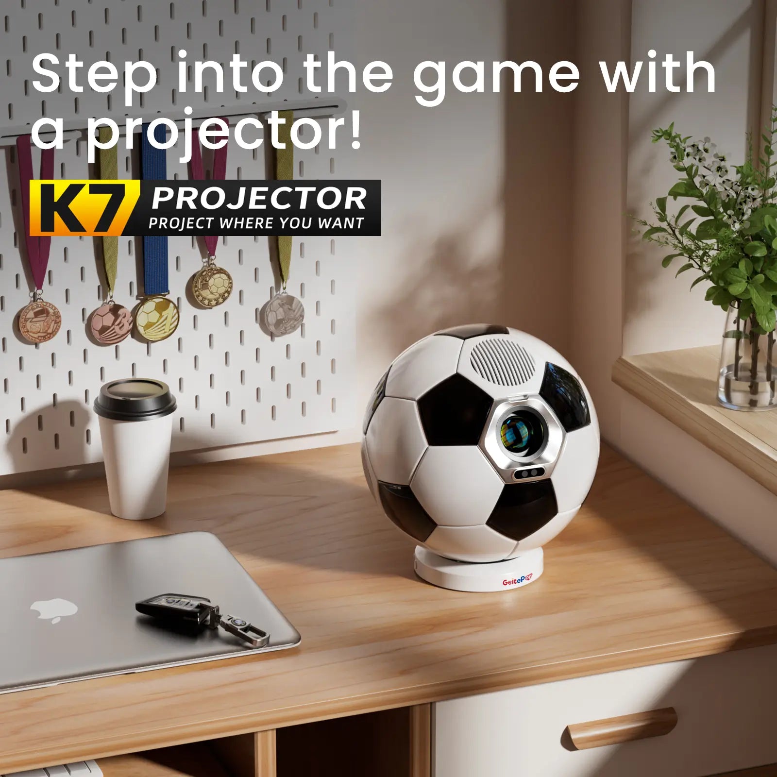 The K7 projector sitting on a desk next to a laptop, with sports medals in the background, illustrating its use for gaming and sports entertainment.