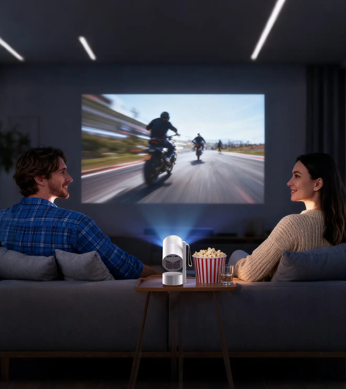 A couple enjoys a movie night at home watching a large screen powered by a small, white portable projector.